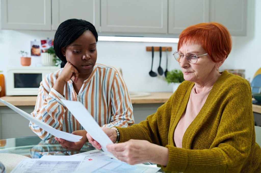 A care coordinator and an older woman going through paperwork at her kitchen table