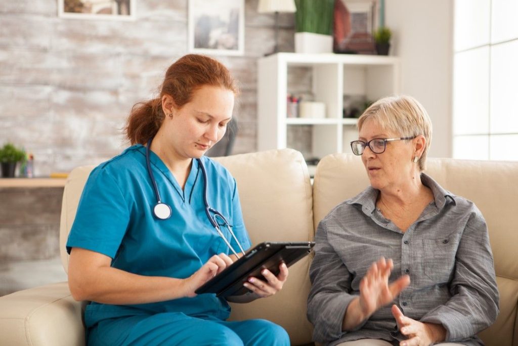 A carer using a tablet to go through a care plan with an older woman on her sofa