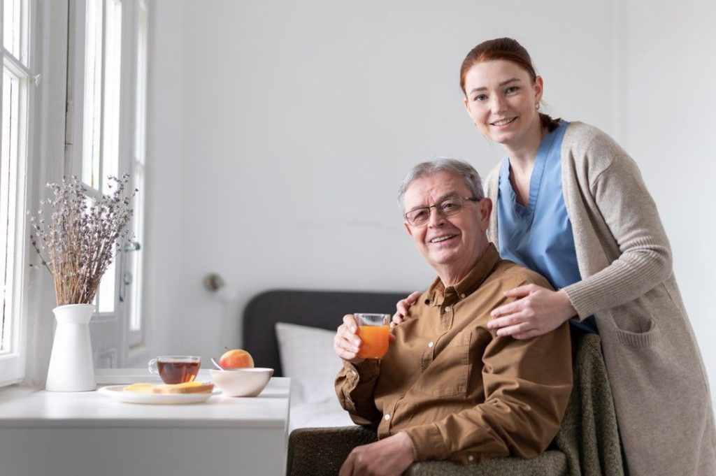 A smiling older man having breakfast at home with his carer beside him