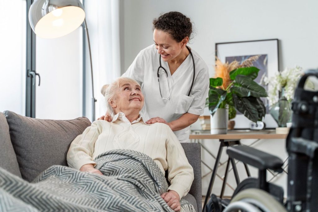 A carer resting her hands on an older woman's shoulders as they smile at each other in her living room