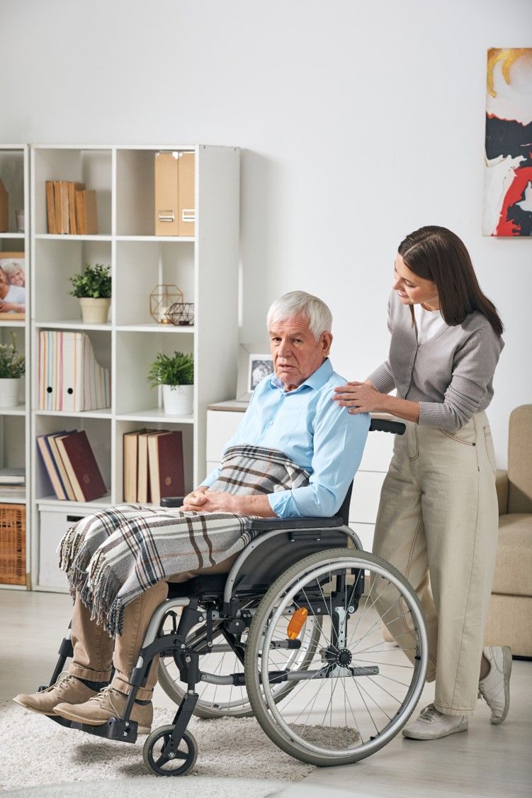 A carer with her hand on the shoulder of an older man in a wheelchair at home