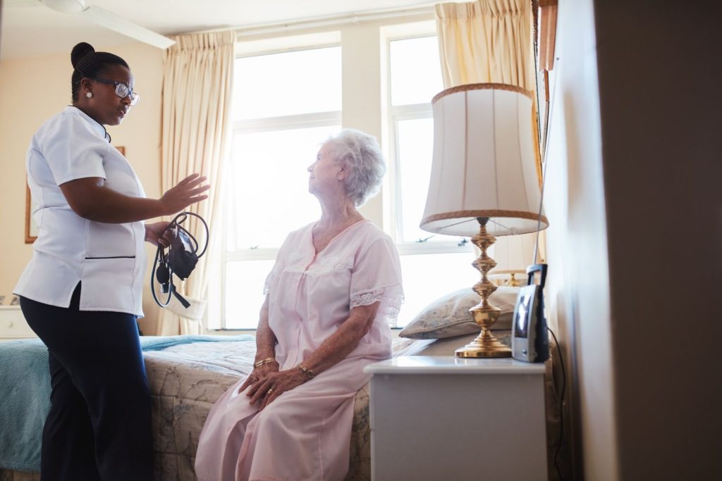 A carer talking with an older woman sitting on her bed during a home visit