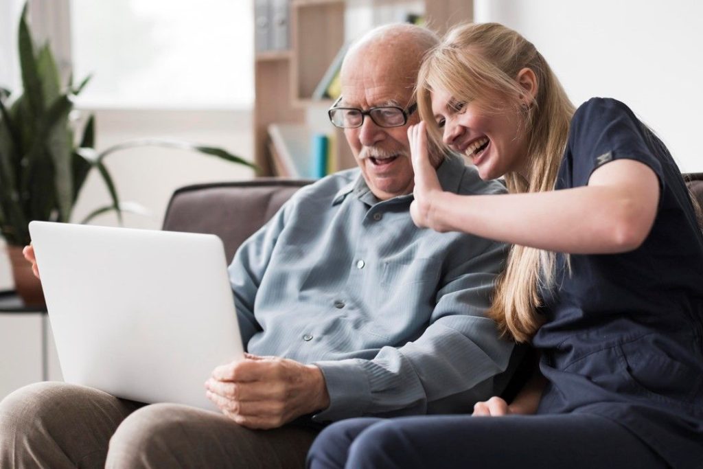 A carer and an older man laughing as they wave on a video call